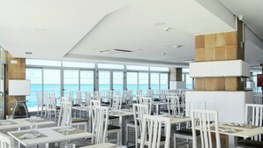 A restaurant with white tables and chairs, large windows, and a view of the sea. - Aluasun Doblemar (San Javier)