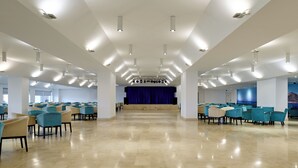 A spacious hall with rows of chairs and a stage with a blue curtain. - Aluasun Doblemar (San Javier)