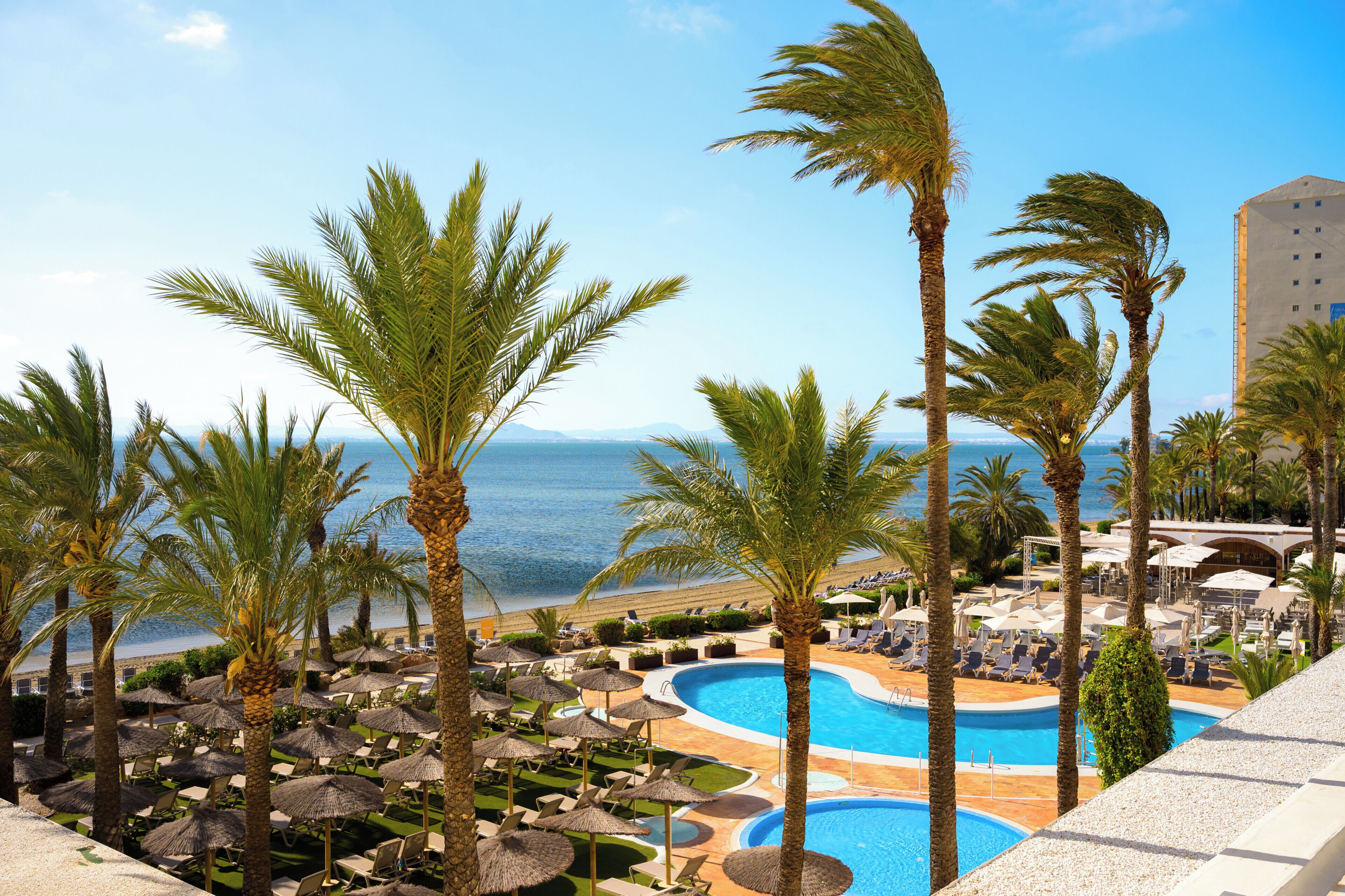 A resort with a pool, palm trees, and a view of the sea.