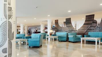 Un hall con sofás color turquesa, mesas blancas y una pared decorativa.