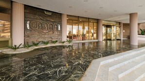 A hotel lobby with a marble floor, a large decorative wall, and a glass entrance. - Aluasun Doblemar (San Javier)