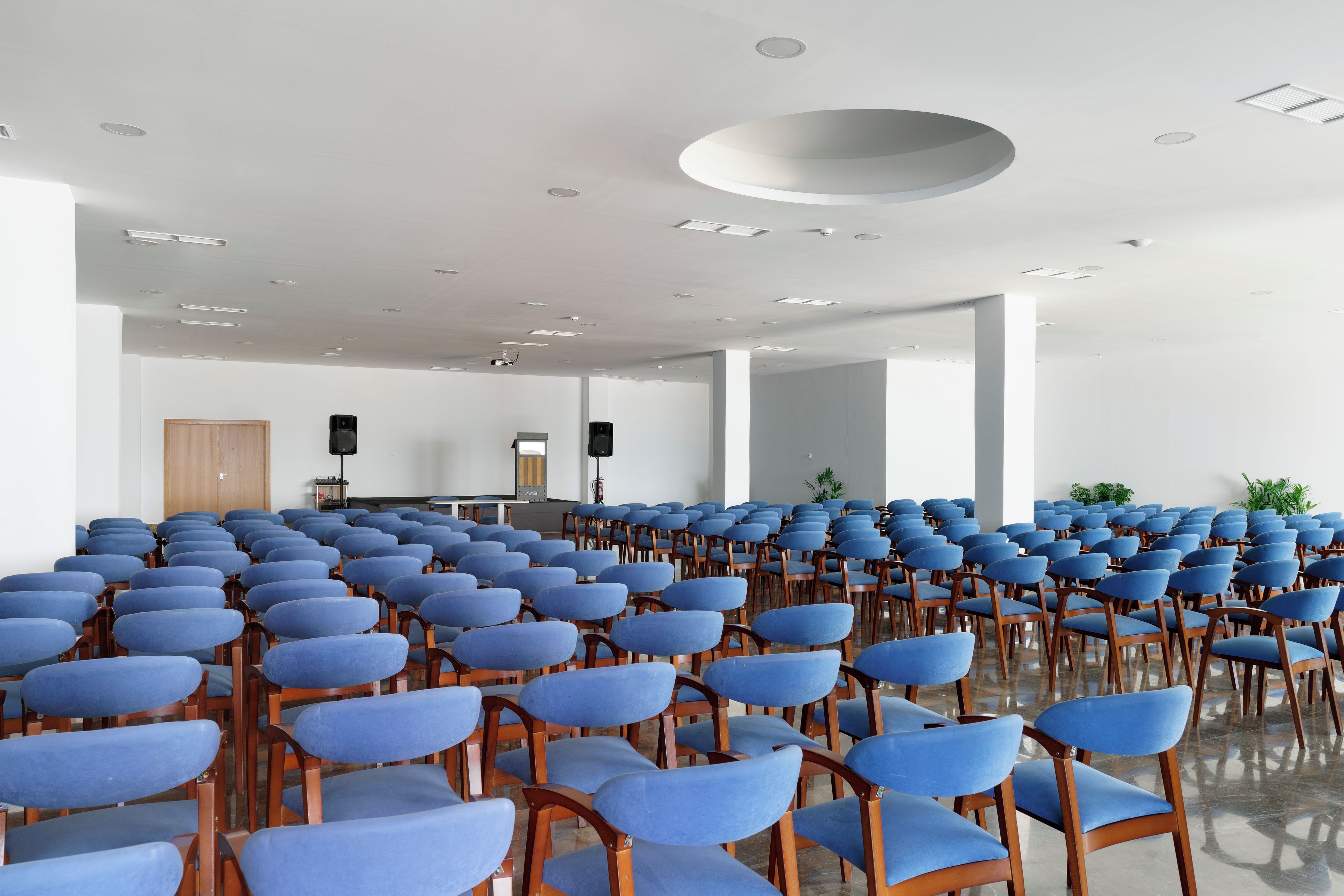 Un salón de conferencias con filas de sillas azules y un atril al frente.