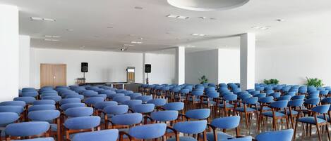 Un salón de conferencias con filas de sillas azules y un atril al frente.