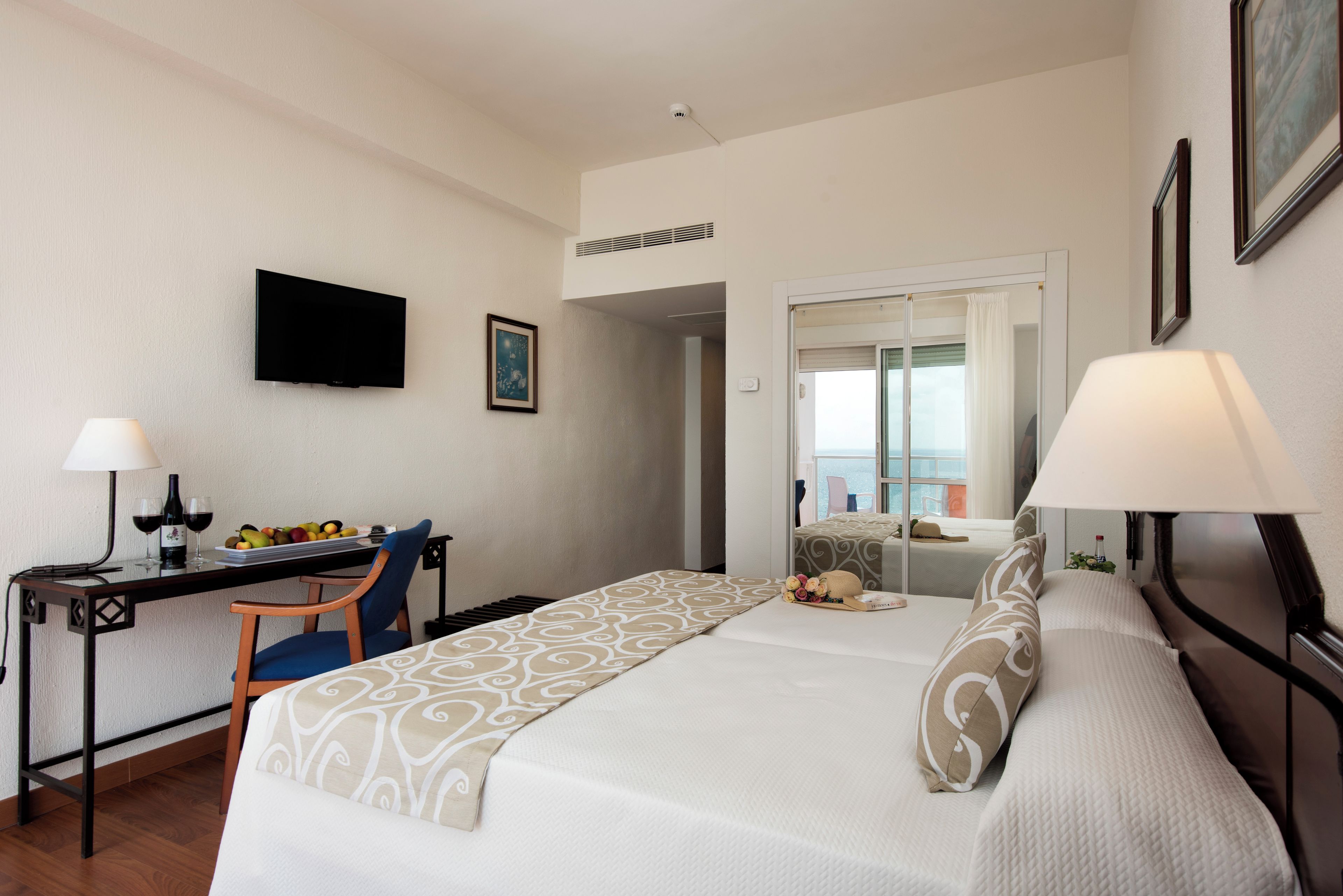 A hotel room with a bed, desk, chair, TV, and a view of the outside.