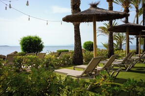 Eine Strandlounge mit Liegest ühlen, Reetdachschirmen und Blick auf das Meer.