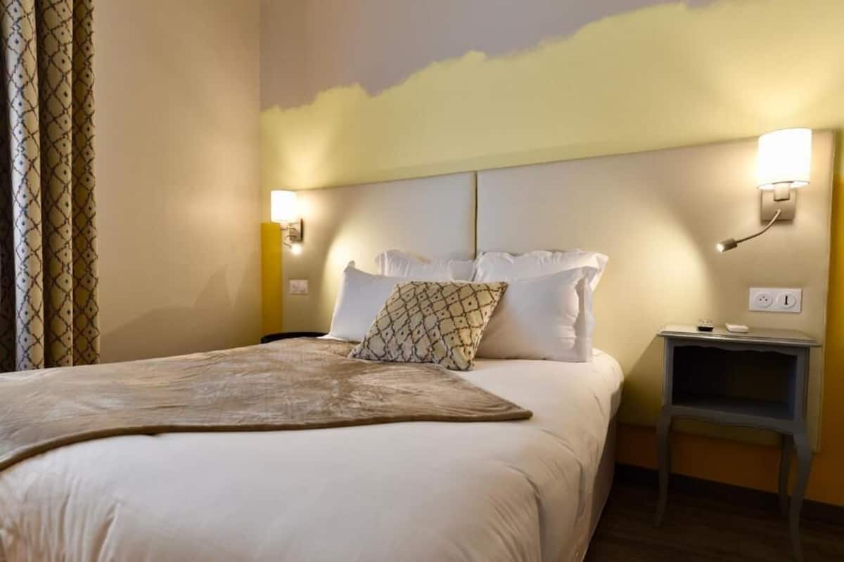A hotel room with a large bed, two bedside tables, and a headboard with wall-mounted lights.