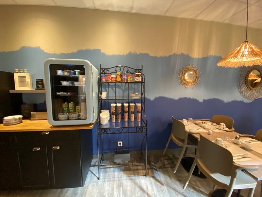 A dining area with a table set for two, a refrigerator, and a shelf with jars.