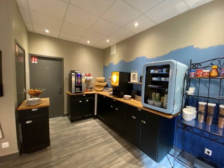 Una cocina moderna con armarios oscuros, encimera de madera y un refrigerador. Hay una estantería con frascos y un lavamanos pequeño.
