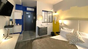 Una habitación de hotel con cama, mesita de noche y televisión en la pared.