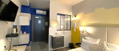 Una habitación de hotel con cama, mesita de noche y televisión en la pared.
