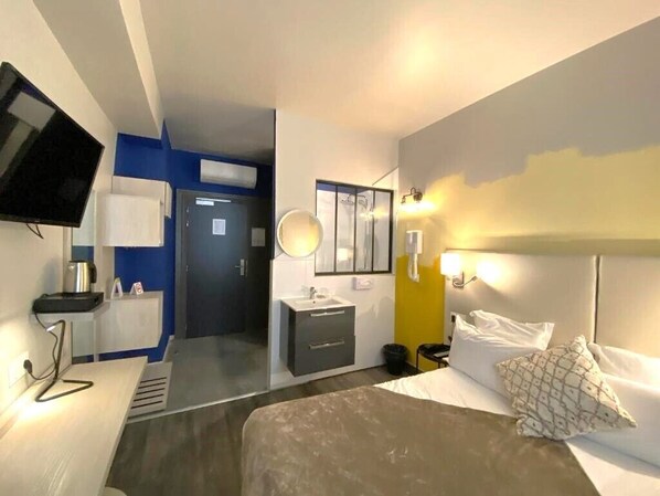 Una habitación de hotel con cama, mesita de noche y televisión en la pared.