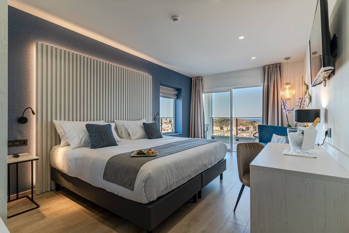 A modern hotel room with a large bed, a desk, and a view of the city.