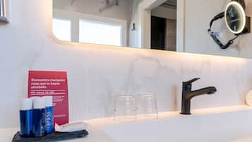 A bathroom with a white marble countertop, a black faucet, and a mirror with a light. There are two clear glasses and a red sign on the wall.