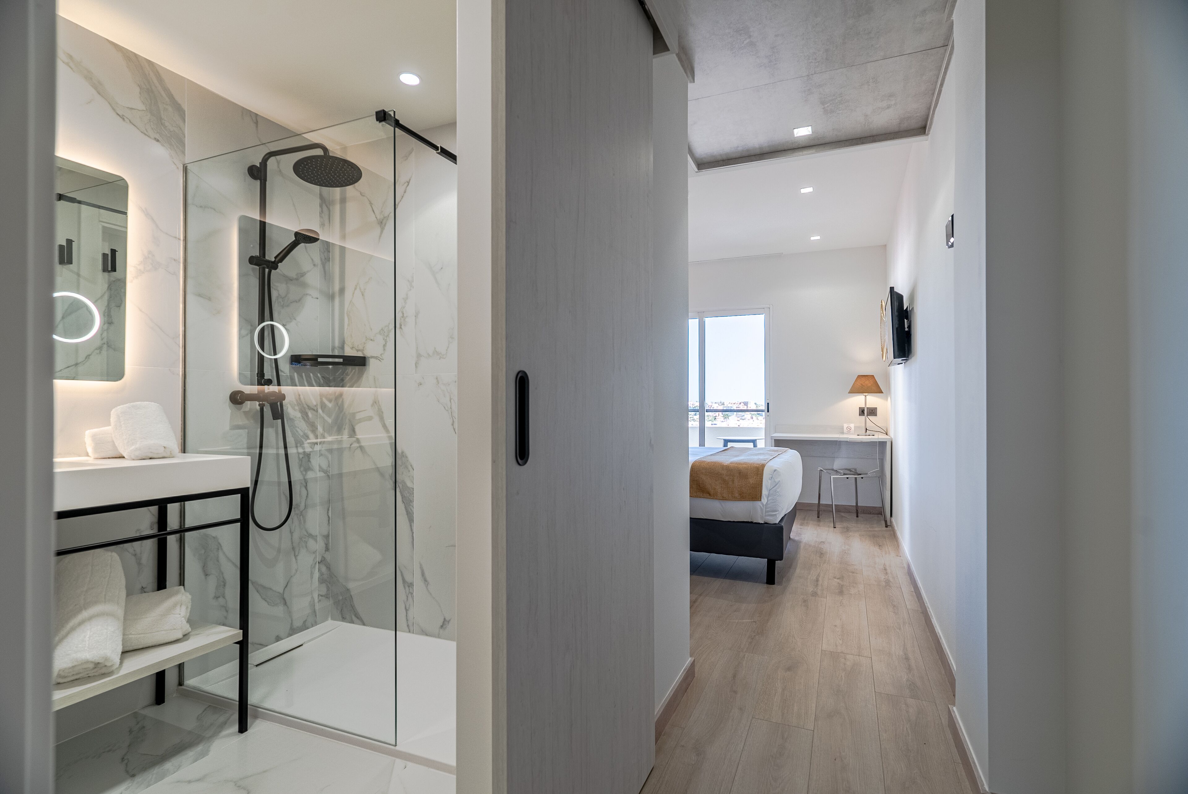 A modern bathroom with a glass-enclosed shower, marble walls, and a white sink.