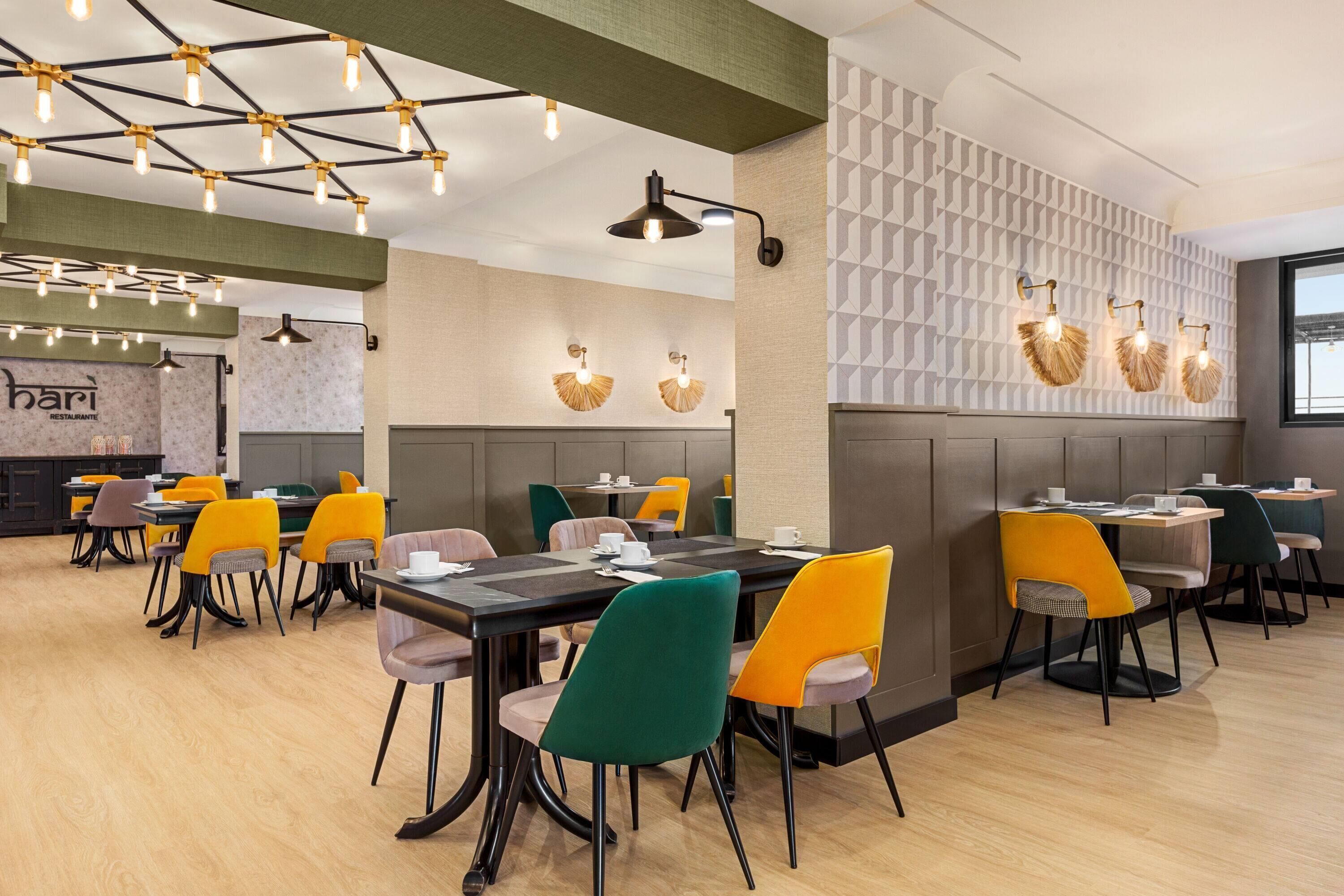 Un restaurante moderno con varias mesas y sillas, una zona de bar e iluminación decorativa en las paredes.