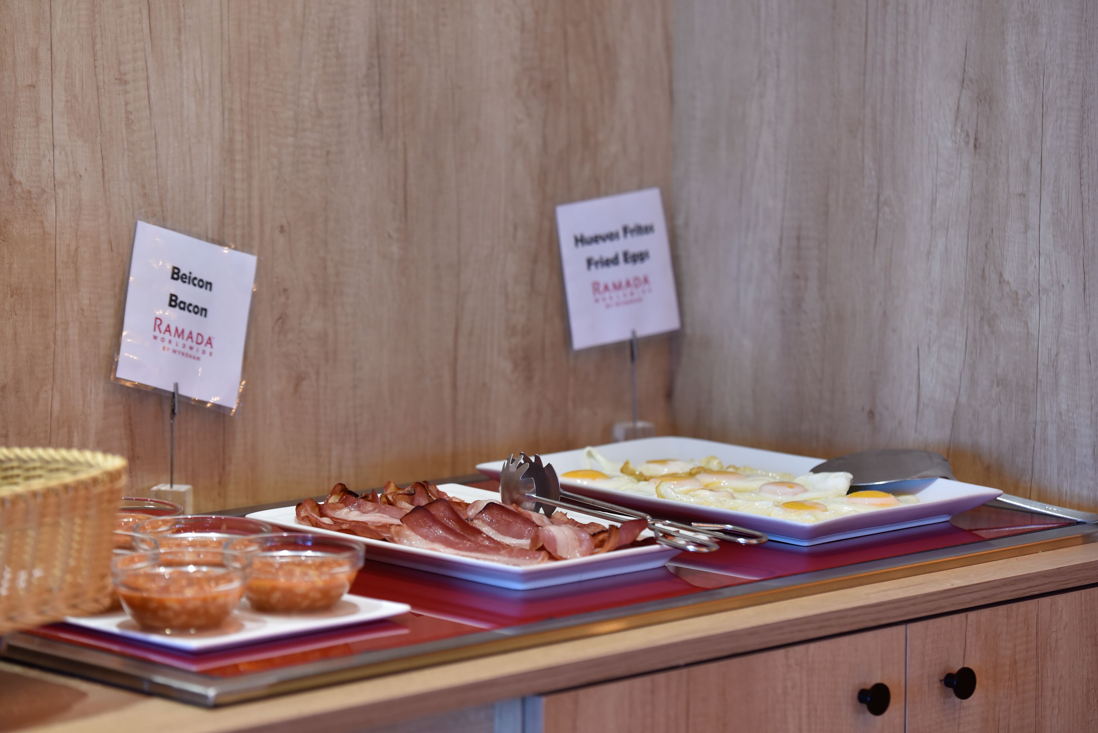 Een ontbijtbuffet met aangeduide gerechten, waaronder spek en gebakken eieren.