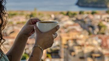 A person holding a cup, with a coastal view in the background.