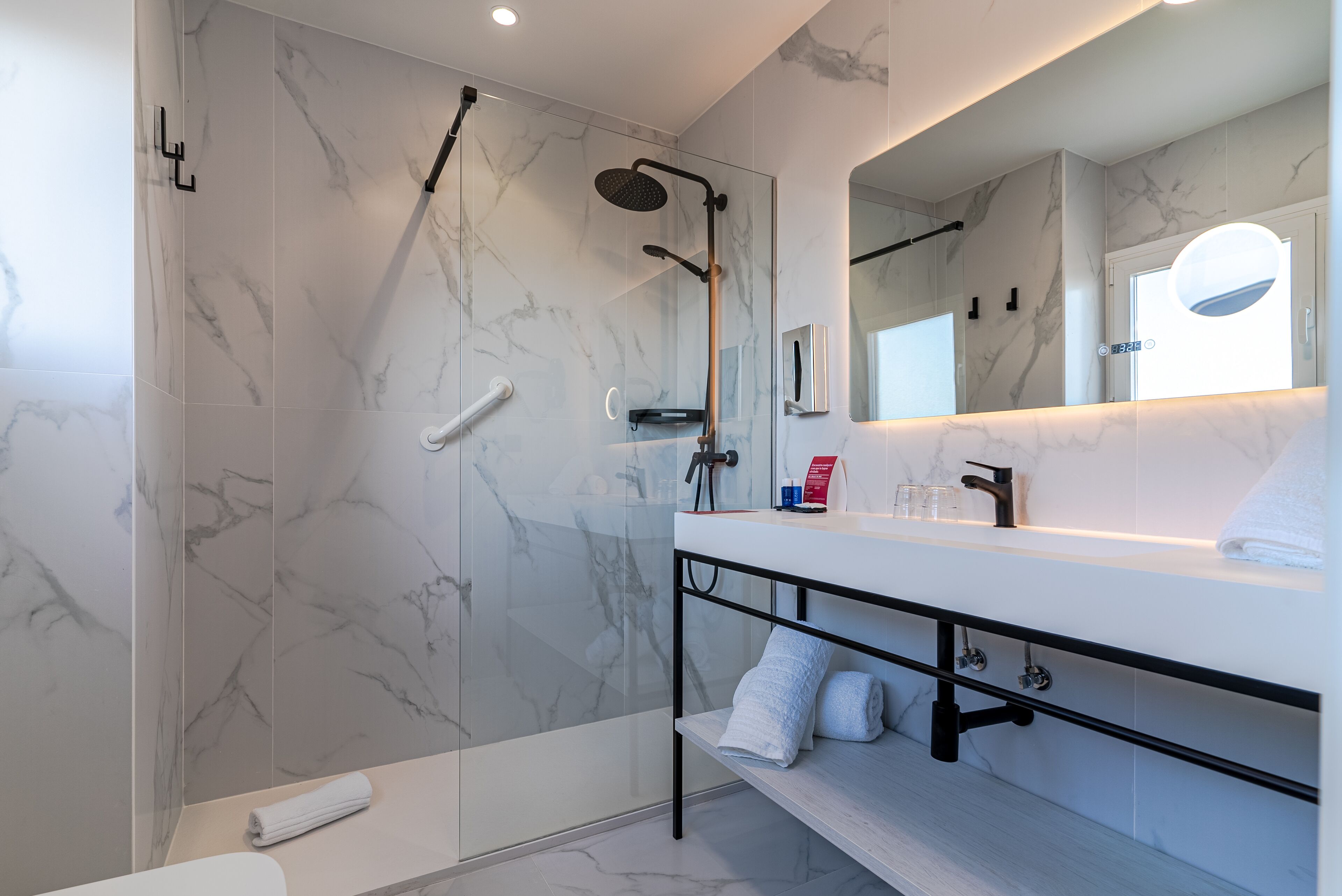 A modern bathroom with a glass-enclosed shower, a white vanity with a mirror, and marble walls.