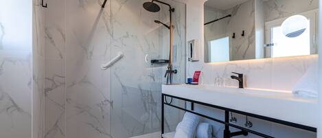 A modern bathroom with a glass-enclosed shower, a white vanity with a mirror, and marble walls.