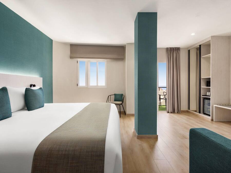 Una habitación de hotel moderna con una cama grande, un escritorio, una silla y vistas al exterior.