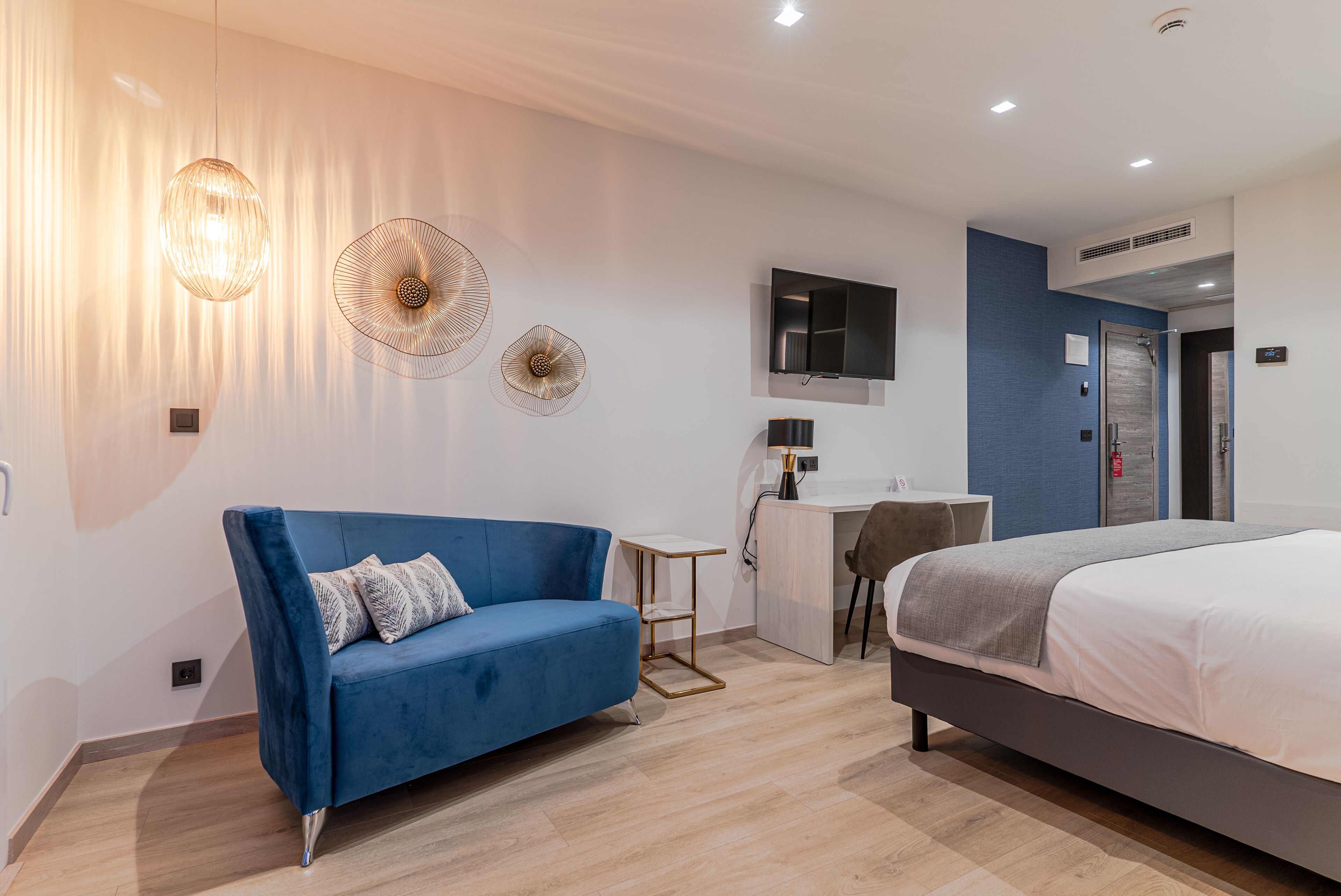 A modern hotel room with a blue sofa, a bed, a desk, and a TV.