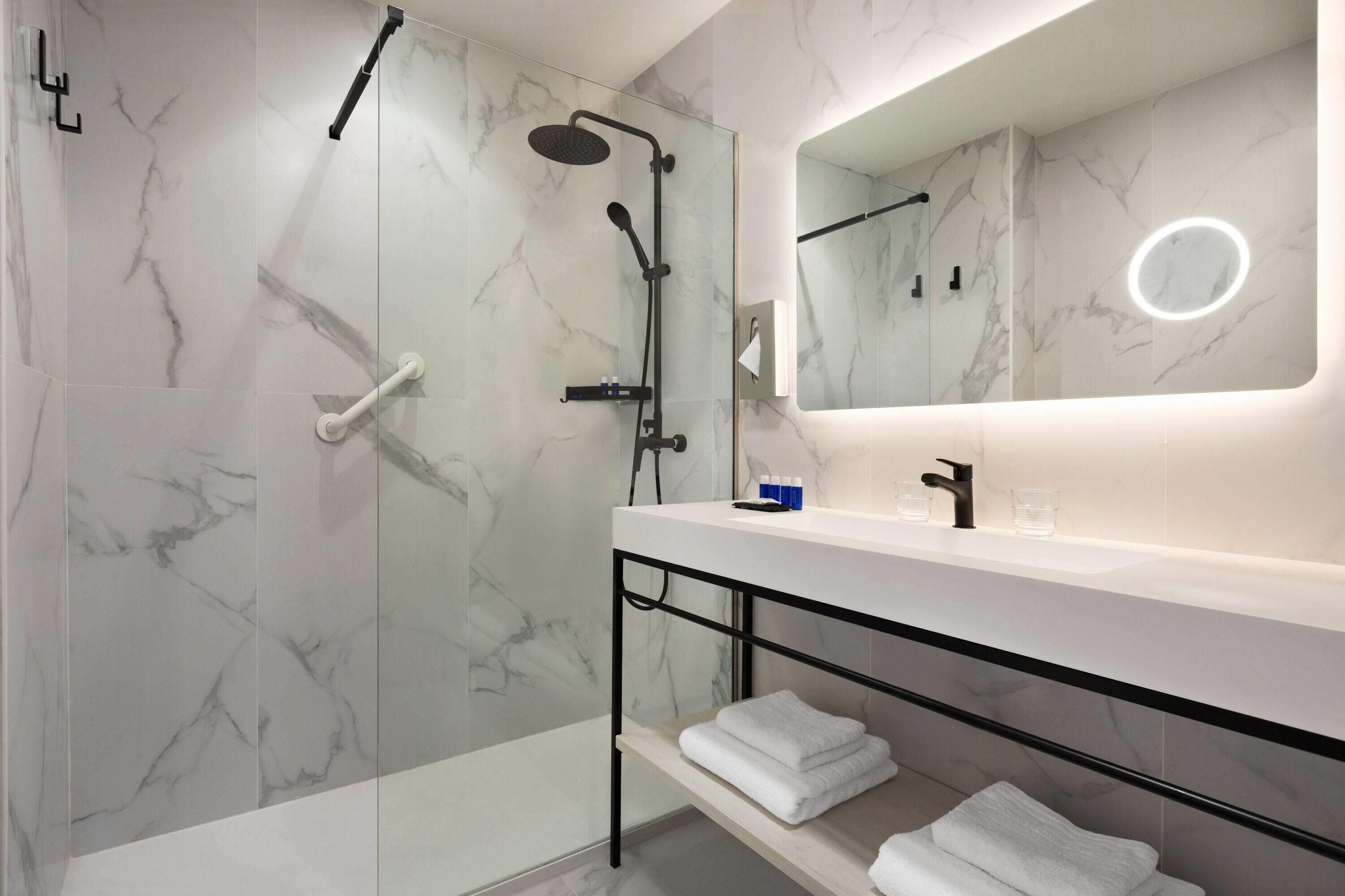 Een moderne badkamer met een marmeren wand, een douche met handdouche, een wastafel met spiegel en een handdoekrek.