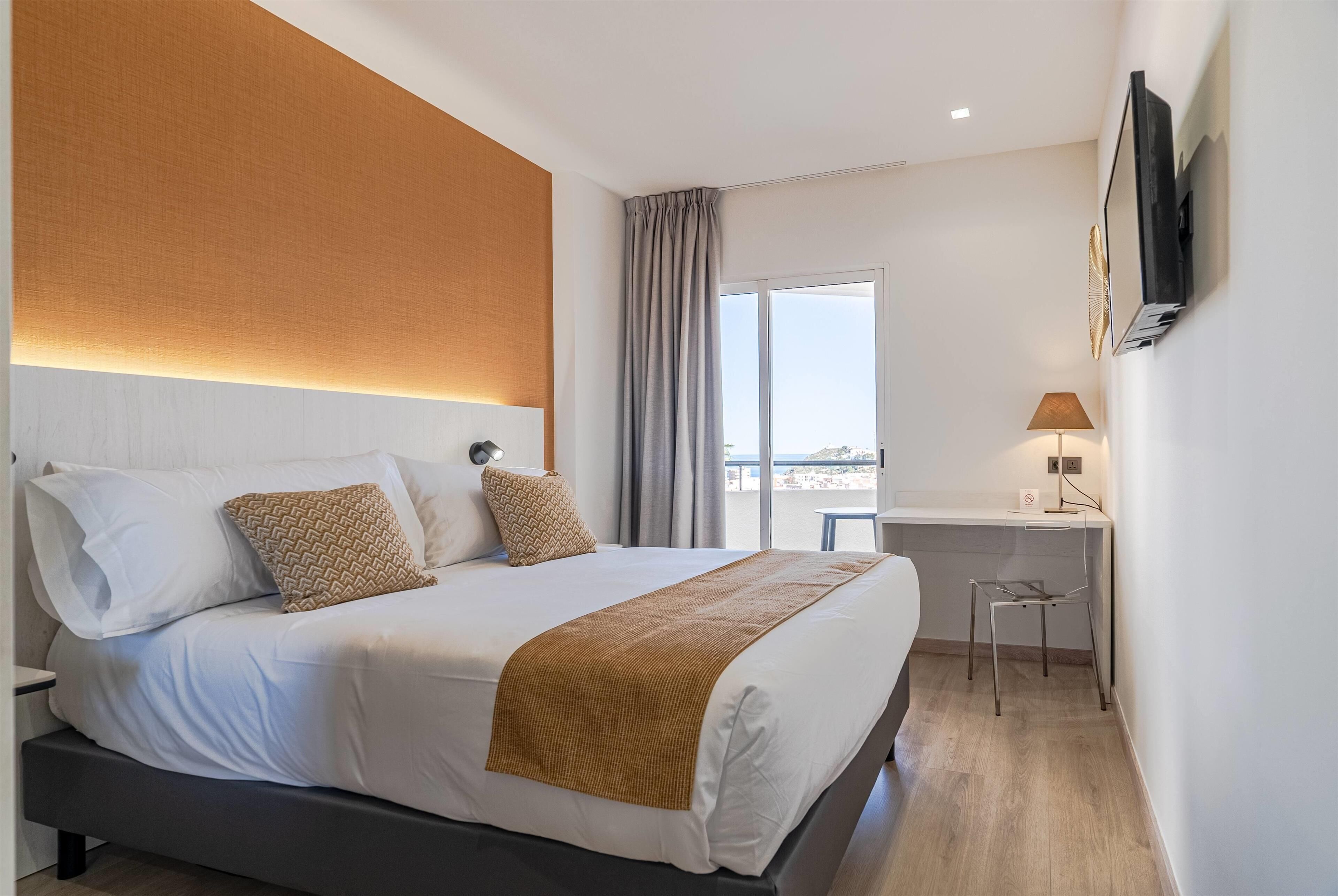 Habitación de hotel con una cama grande, un escritorio, una silla y un televisor montado en la pared.