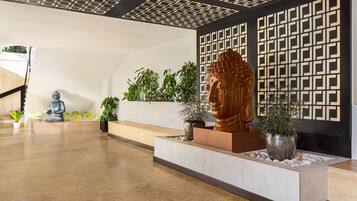 Un hall d’entrée moderne agrémenté d’une grande statue de Bouddha, de plantes en pot et d’un motif géométrique sur le mur.
