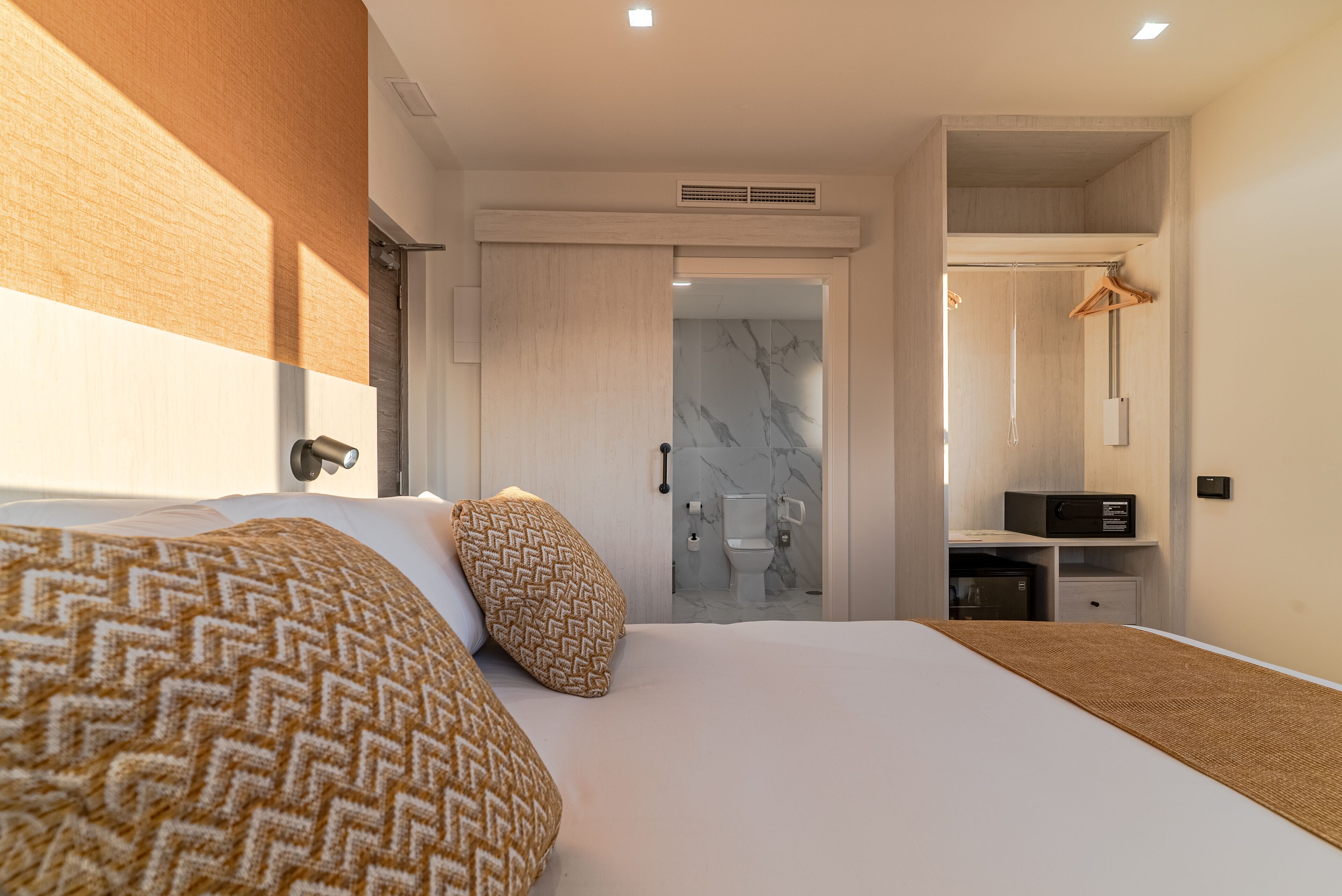 A modern hotel room with a large bed, a walk-in closet, and a bathroom with a marble shower.