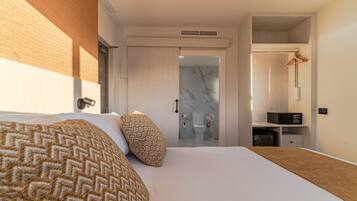 Una habitació d'hotel moderna amb un llit gran, un armari encastat i un bany amb plat de dutxa de marbre.
