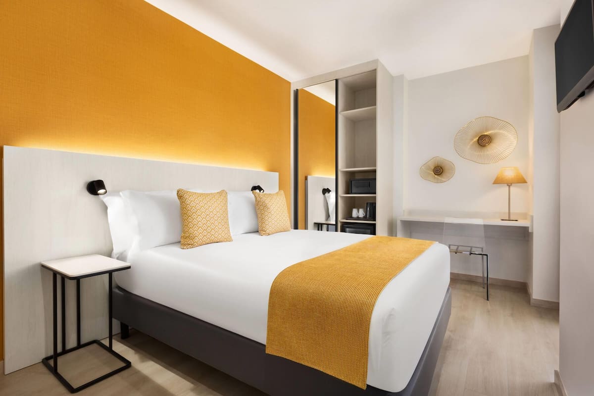A modern hotel room with a large bed, bedside tables, a desk, and a TV mounted on the wall.