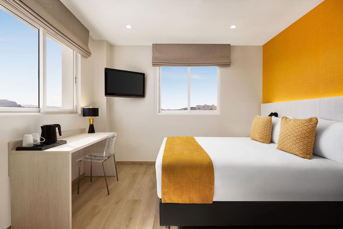 A hotel room with a bed, a desk, a chair, a TV, and a window with a view.