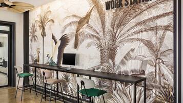 Un espacio de trabajo con un mural de plantas tropicales y un monitor sobre un escritorio.