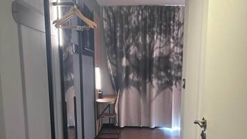 Une chambre d’hôtel avec un plancher en bois, une chaise, une table, un porte-manteau mural et un rideau orné d’un motif d’arbres.