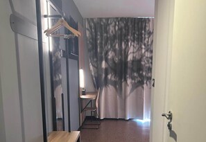 A hotel room with a wooden floor, a chair, a table, a hanging coat rack, and a curtain with a tree pattern. - B&B HOTEL Amélie-les-Bains Centre (Amelie-les-Bains-Palalda)