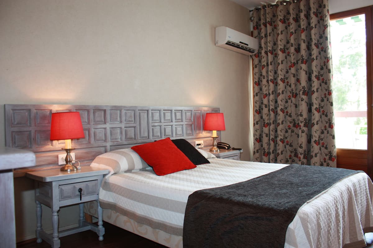 A neatly made bed with a striped bedspread, two bedside lamps, a nightstand, and a floral curtain.