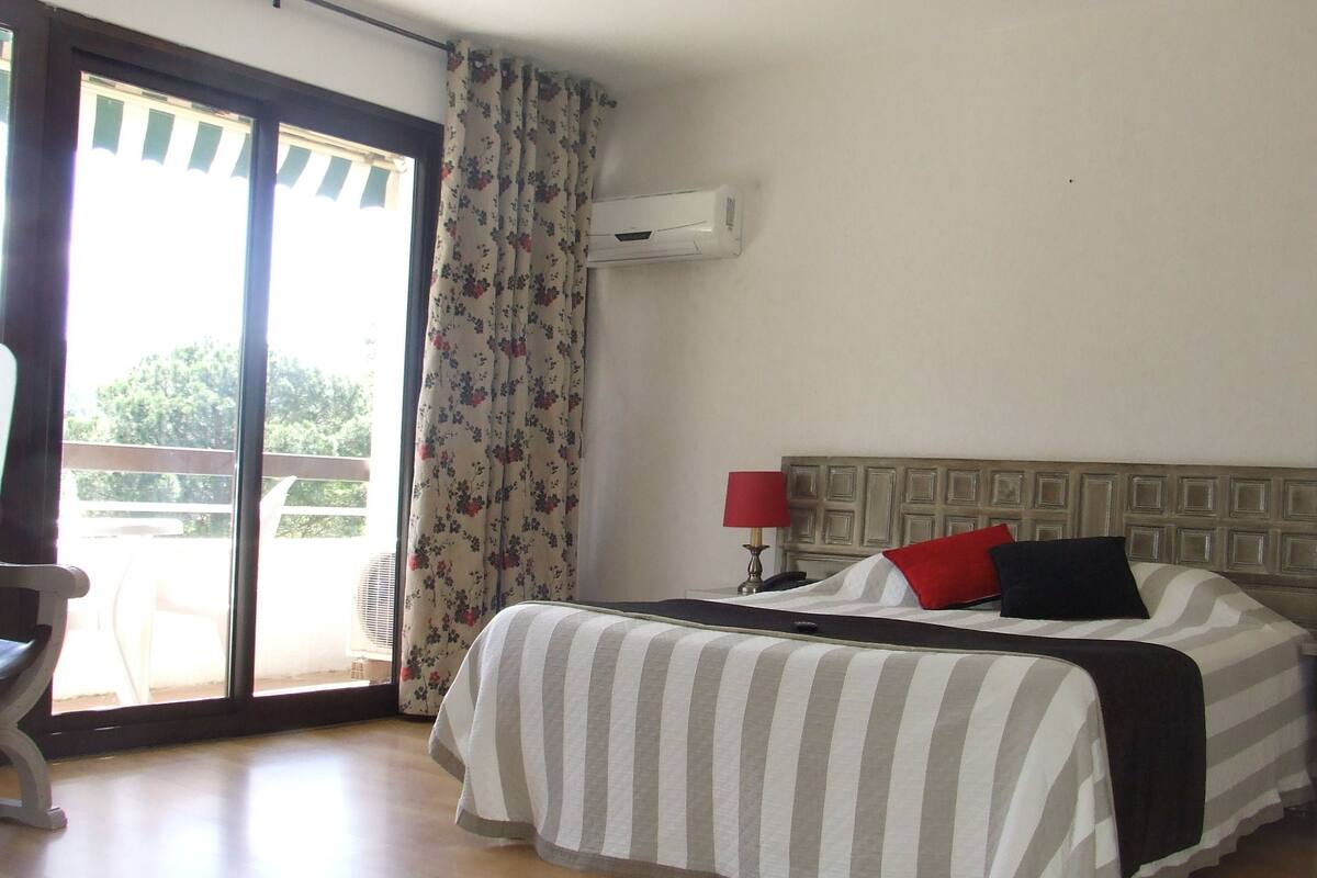 A hotel room with a bed, a nightstand, a lamp, and a window with curtains.