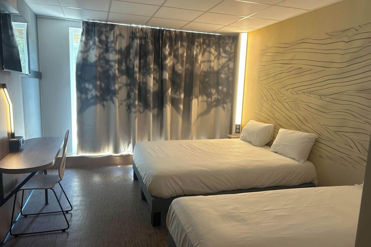 A hotel room with two beds, a desk, a chair, and a TV.