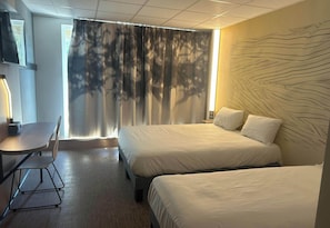 A hotel room with two beds, a desk, a chair, and a TV.