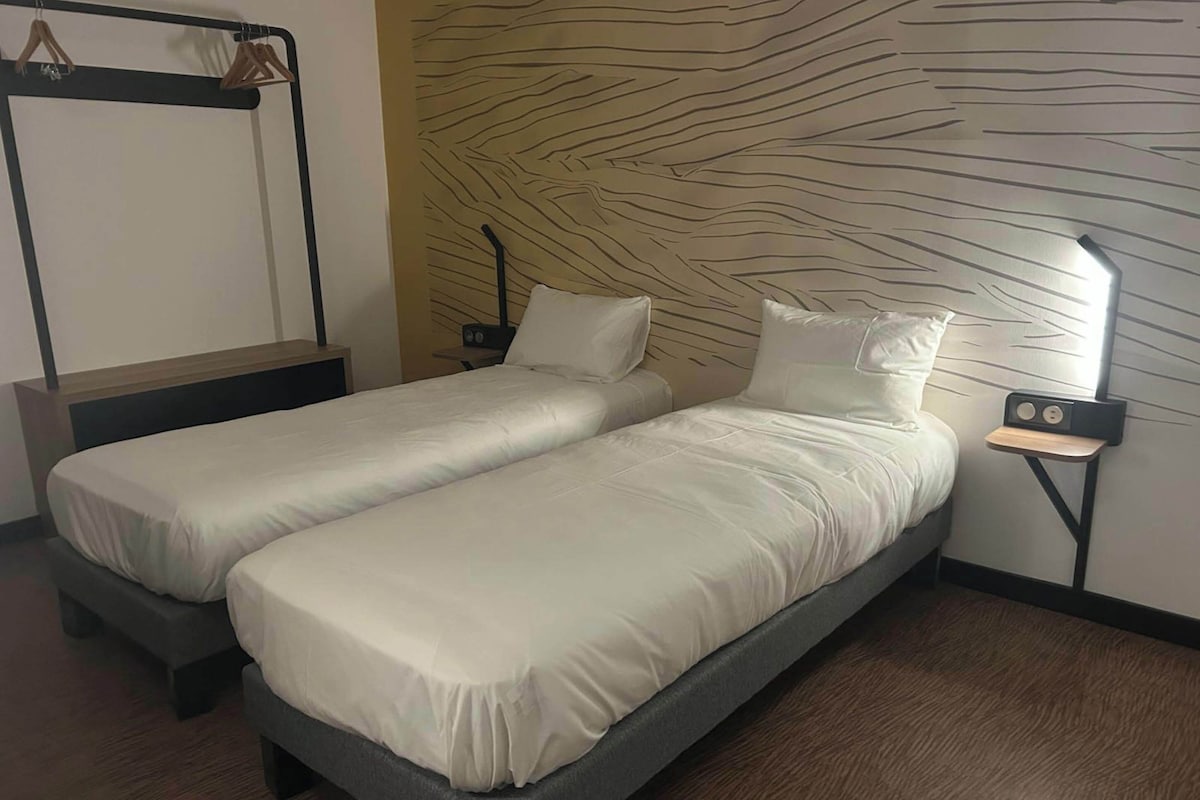 A twin room with two single beds, a wooden nightstand, a mirror, and a patterned wall.