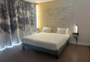 A modern bedroom with a large bed, a wall-mounted light, and a curtain. - B&B HOTEL Amélie-les-Bains Centre (Amelie-les-Bains-Palalda)