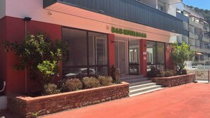 A hotel with a red facade, large windows, and a balcony. - B&B HOTEL Amélie-les-Bains Centre (Amelie-les-Bains-Palalda)