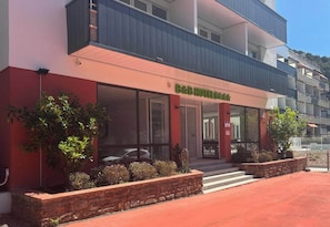 A hotel with a red facade, large windows, and a balcony.