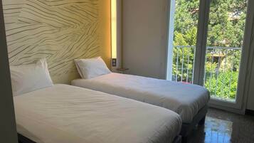 Une chambre d’hôtel avec deux lits, une grande fenêtre et une vue sur la verdure environnante.