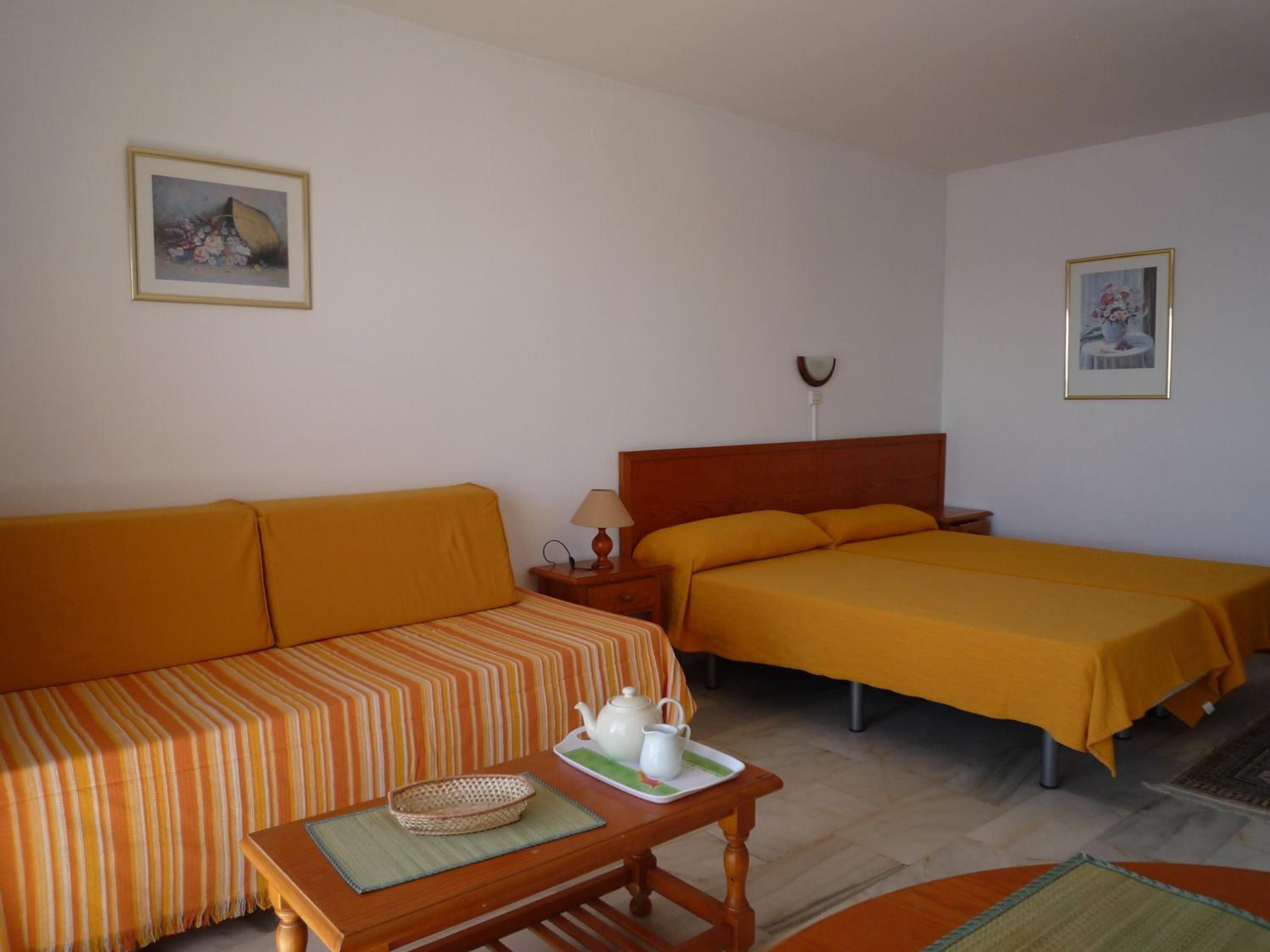 Una habitación con sofá, cama, mesita de noche con lámpara y bandeja con tetera.