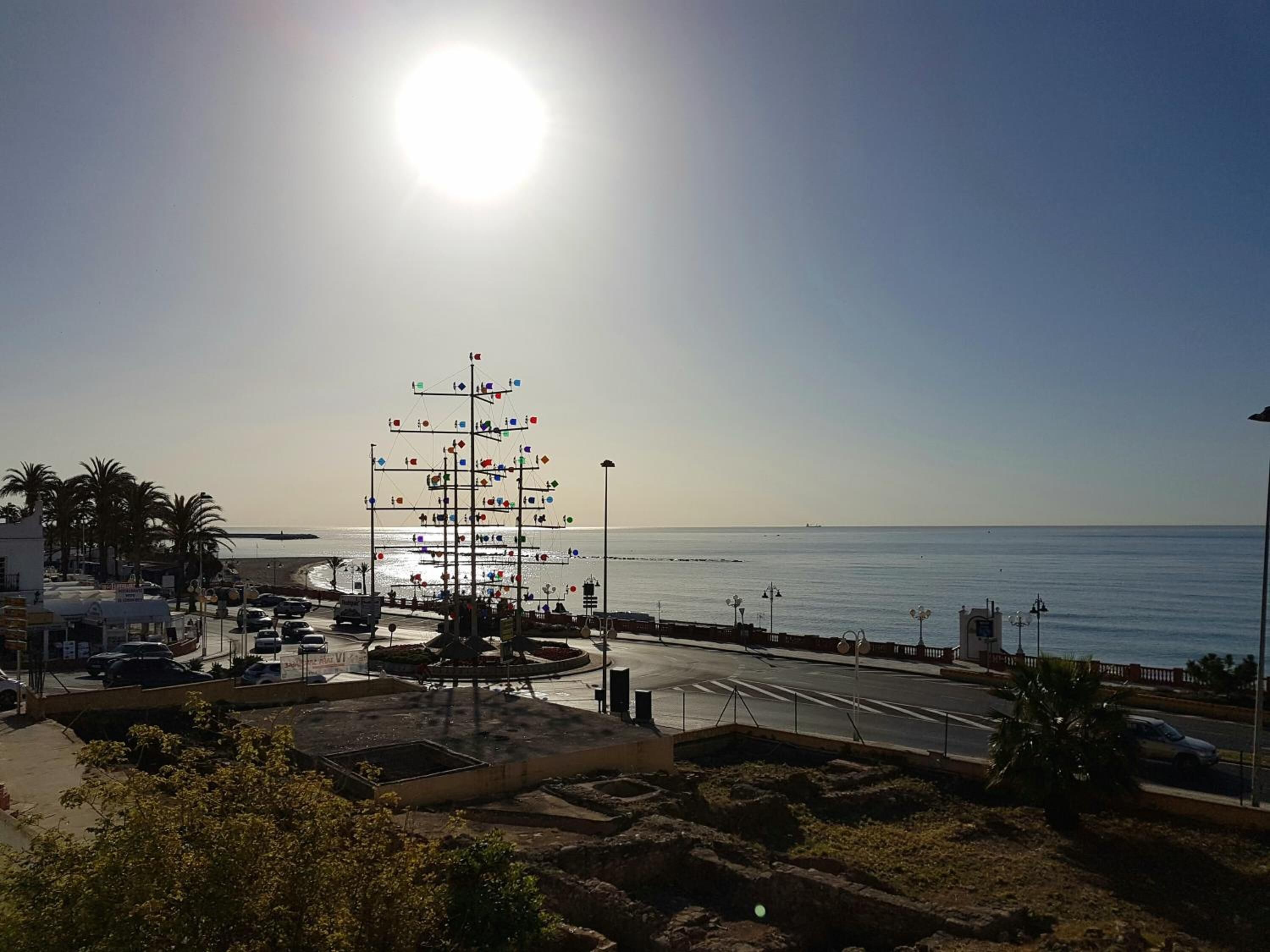 A coastal view with a clear sky, a beach, and a large decorative structure in the center.
