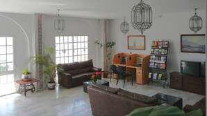 Un salon spacieux avec un canapé en cuir marron, un bureau en bois avec deux chaises, une bibliothèque et un téléviseur.
