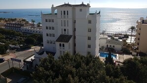 Un grand immeuble blanc, doté de nombreuses fenêtres et d’un balcon, situé près d’une plage et offrant une vue dégagée sur l’océan.