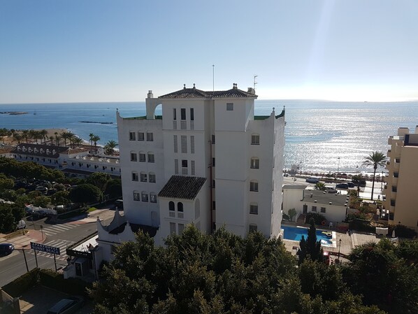 A tall white building with multiple windows and a balcony, located near a beach with a clear view of the ocean. - Apartamentos Turísticos Sunny Beach (Benalmádena)