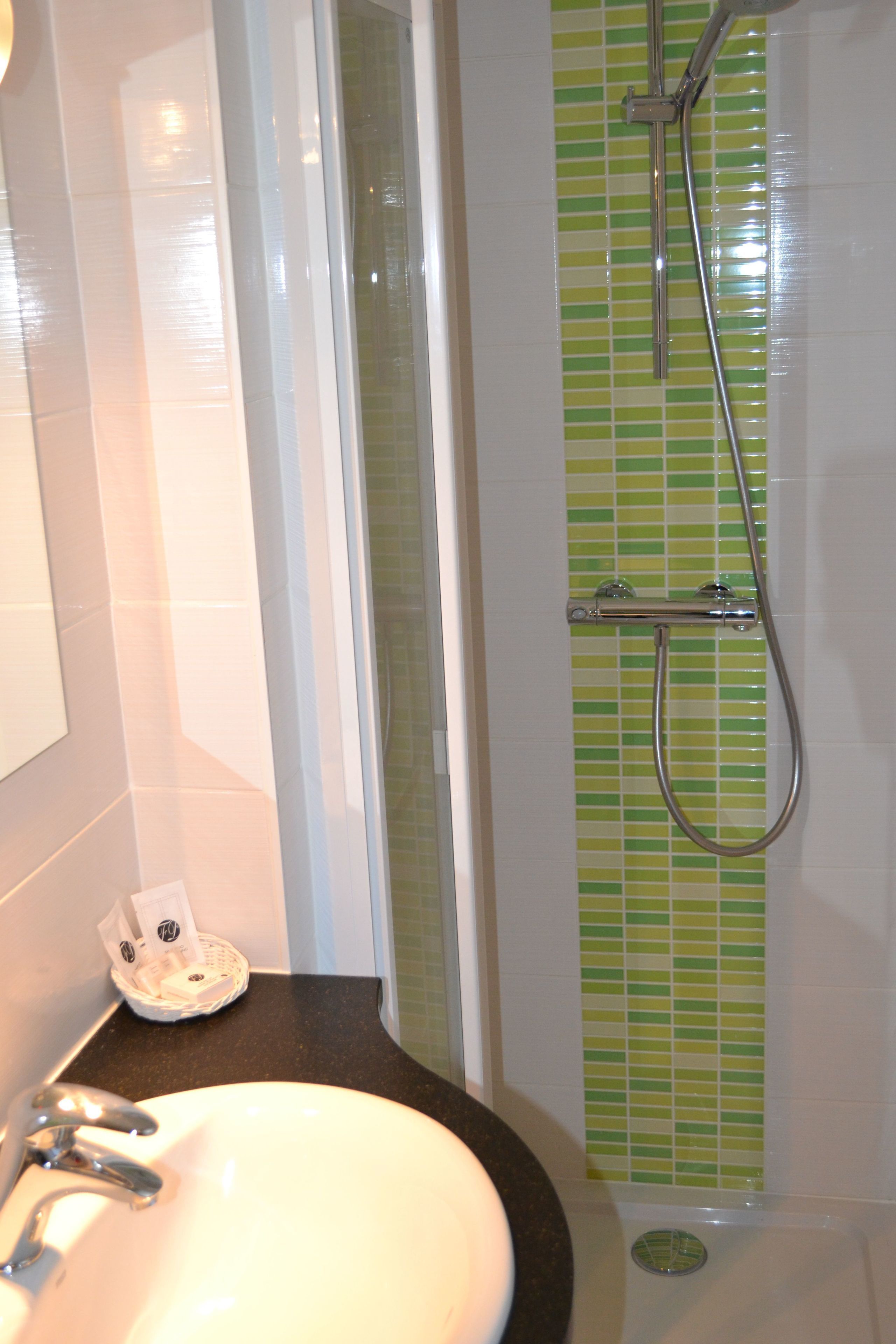 A bathroom with a white sink, a shower with a green tiled wall, and a white door.